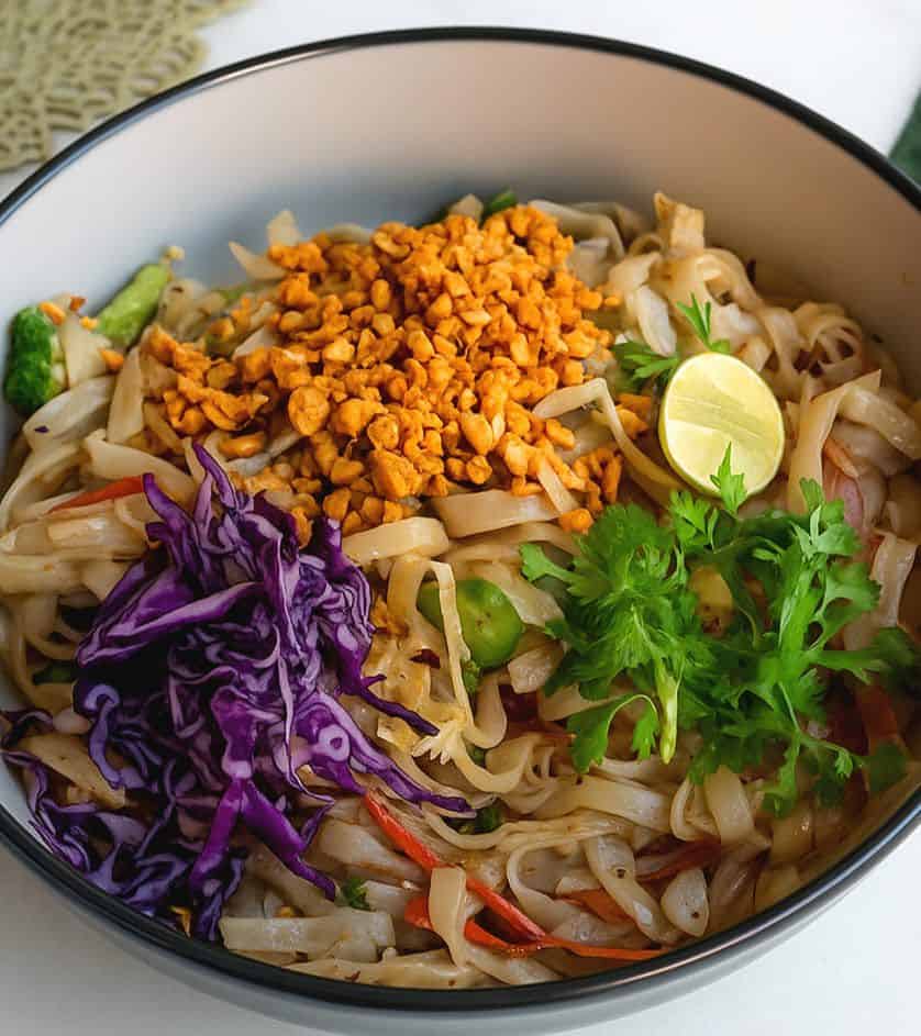 Healthy millet noodle bowl topped with crunchy roasted millet, shredded purple cabbage, fresh cilantro, colorful vegetables, and a lime wedge.